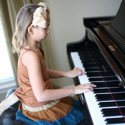 side view of a Caucasian young girl concentrating on playing the piano while wearing a monkey tail and ears