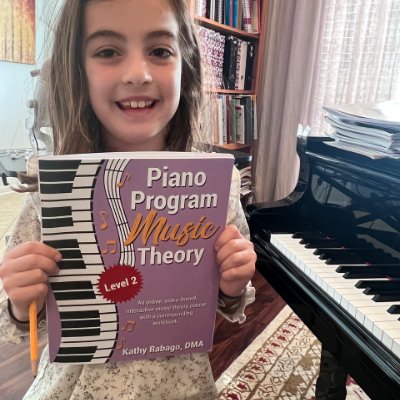 A happy young pre teen sitting next to her piano holding a music theory book