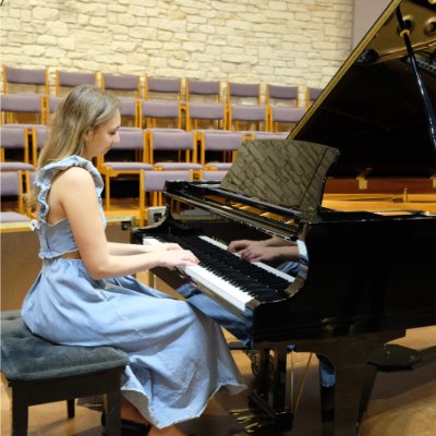 Side view of a teenage girl wearing a prom dress playing a grand piano in a concert hall