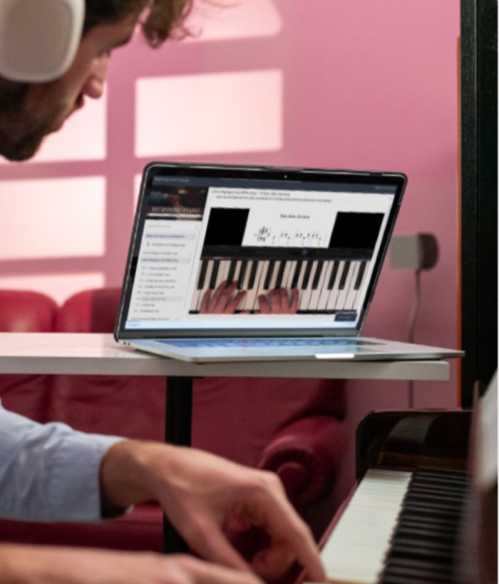 man with headphones learning the piano using a course video on the laptop